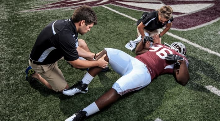 Therapist treating a football player's leg on the field